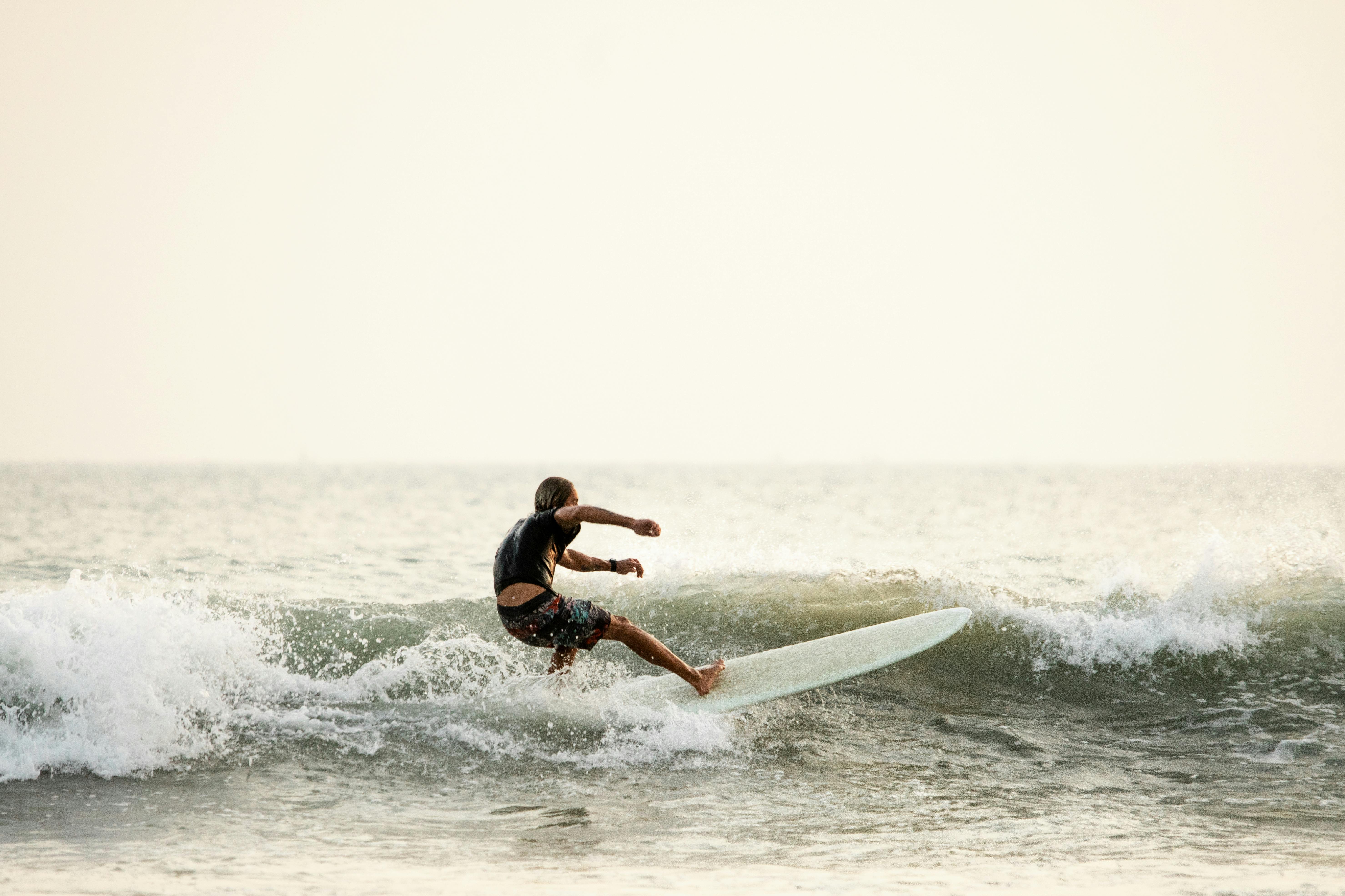 pexels-photo-7952882-7952882 Side view of anonymous male surfer in swimwear standing on surfboard on wavy seawater and balancing while practicing surfing against white sky